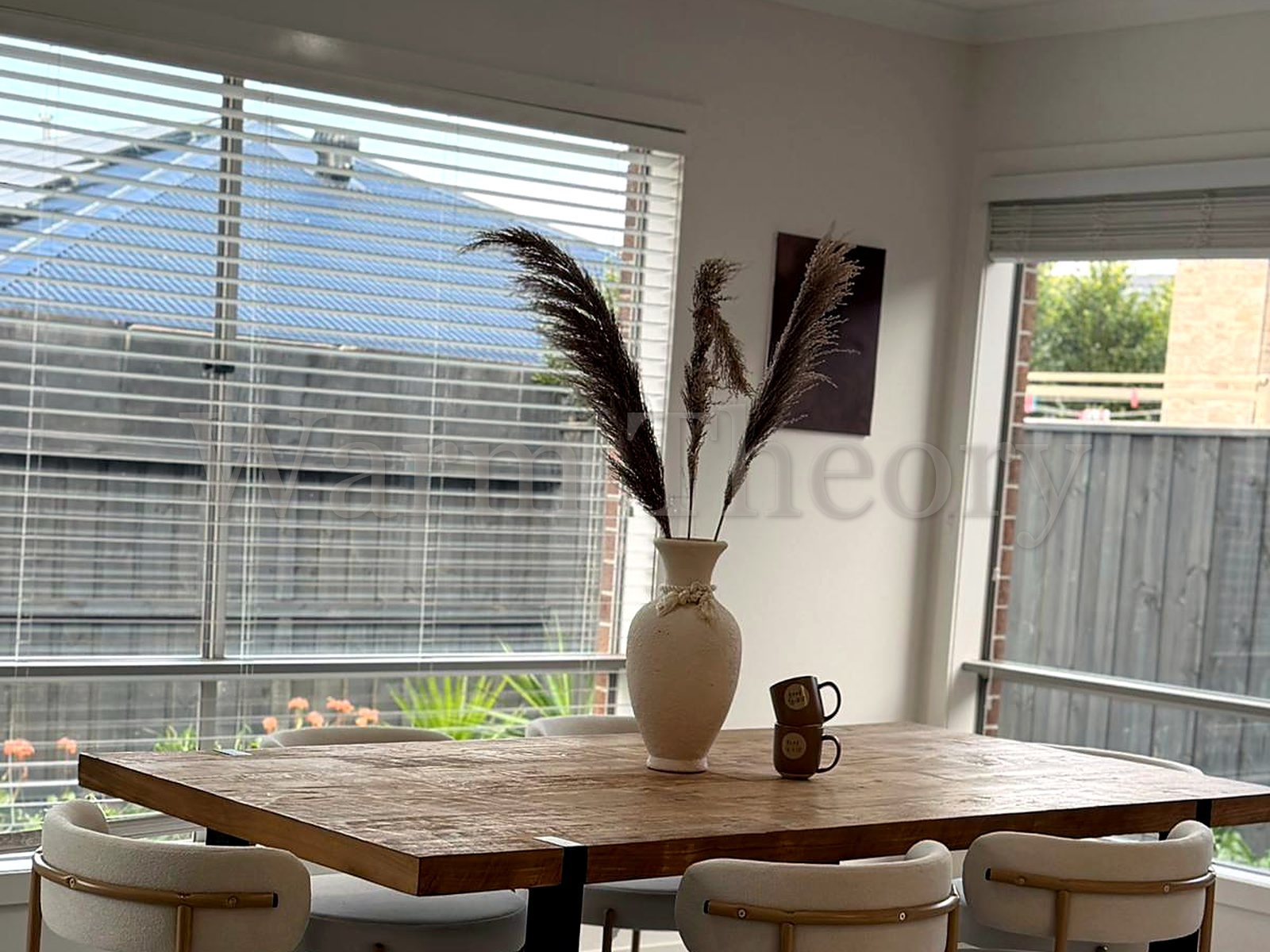 Dining area styled with a timber table, cream boucle and gold-framed chairs, and pampas grass in a cream vase