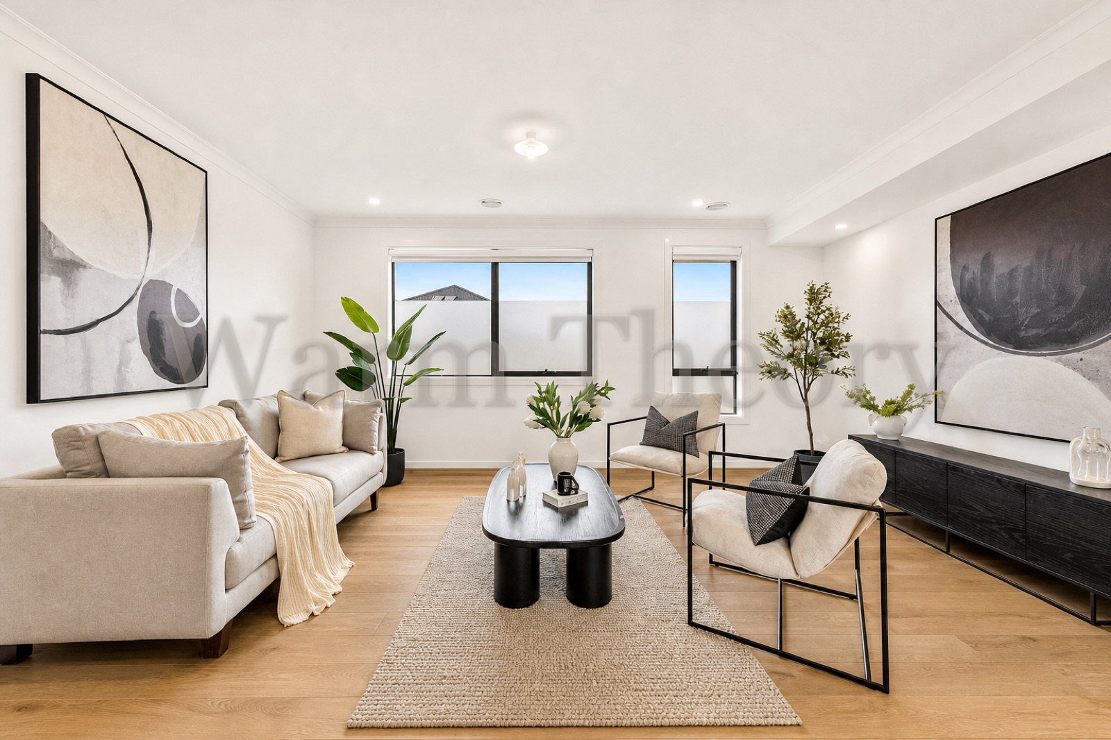 Staged living room with two cream sofas, a black oval coffee table, large abstract artworks, and warm oak floors